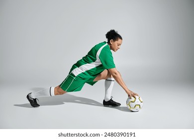 Female athlete in green jersey stretching on white studio floor, reaching for soccer ball. - Powered by Shutterstock