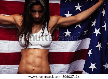 Female athlete holding American flag looking down. Healthy young woman wearing sports clothing with United States of American flag.