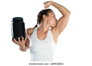 Female athlete holding supplement jar while kissing biceps against white background - Powered by Shutterstock