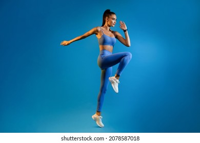 Female Athlete Jumping Exercising During Training Over Blue Studio Background, Looking Aside. Fitness Workout And Sport Motivation Concept. Full Length, Side View - Shutterstock ID 2078587018