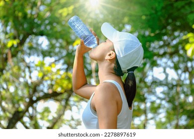 Female athlete lifts a bottle of drinking water in a clean bottle in hot weather with very sunny natural green background. Health and hydration concepts - Powered by Shutterstock