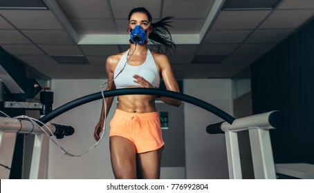 Female Athlete With Mask Running On Treadmill To Analyze Her Fitness Performance. Runner Testing Her Performance In Sports Science Lab.