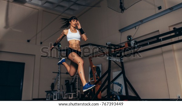 Female athlete with
motion capture sensors on her body running in biomechanical lab.
Recording the movement and performance of sportswoman in sports
science lab.