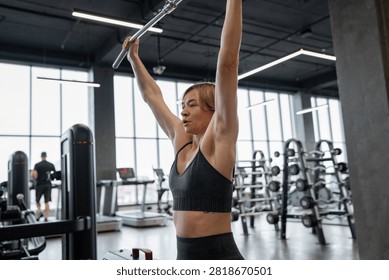 Female athlete performing lat pulldown on cable machine in modern gym from rear view, showing back muscles, focused posture, controlled grip, short hair, sports bra