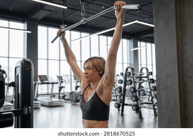 Female athlete performing lat pulldown on cable machine in modern gym from rear view, showing back muscles, focused posture, controlled grip, short hair, sports bra