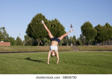 A female athlete performs a cartwheel on a grassy field. - Powered by Shutterstock