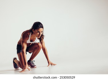 Female athlete in position ready to run over grey background. Determined young woman ready for a sprint.