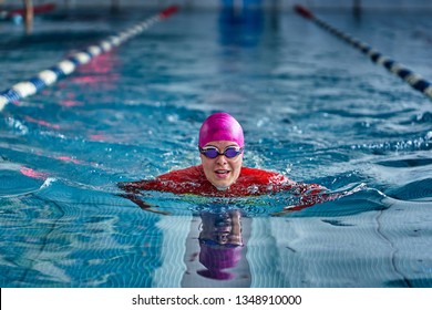 Female athlete in a red-yellow swimsuit is swimming in the style of breaststroke. Splashes of water scatter in different directions. - Shutterstock ID 1348910000