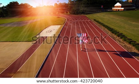 Female athlete running with American flag over head on track