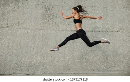 Female athlete running and jumping. Side view of flexible female athlete exercising outdoors. - Shutterstock ID 1873179118