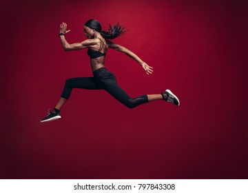 Female athlete running and jumping. Side view shot of healthy african woman working out against red background.
