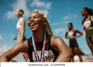 Female athlete smiling after winning a race with other competitors in background. Sportswoman with medal celebrating her victory at stadium., fotografie de stoc