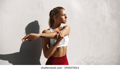 Female athlete stretching arms, prepare for morning run. Female runner workout in sport clothing, do jogging training outdoors in leggings and crop top, prepare for exercises