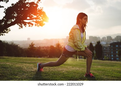 Female athlete stretching legs for warming up before running in city park on sunset or morning. Brunette  sporty woman exercising outdoor. - Powered by Shutterstock