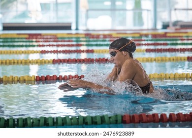 Female athlete swimming in breaststroke style in the pool lane, stroking, immersing, and lifting out of the water to breathe. - Powered by Shutterstock