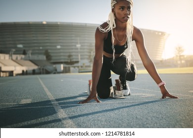 Female athlete taking position on her marks to start off the run. Female runner practicing her sprint on an all-weather running track in a stadium. - Powered by Shutterstock