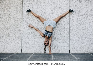 Female athlete in training clothes doing an acrobatic move turning upside down outdoors. Acrobatic fitness woman balancing upside down on one hand with legs in air.