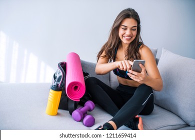 Female athlete using a mobile phone in bed. Woman likes her active life. Beautiful woman preparing for gym. Young woman ready for exercise, checking smartphone 