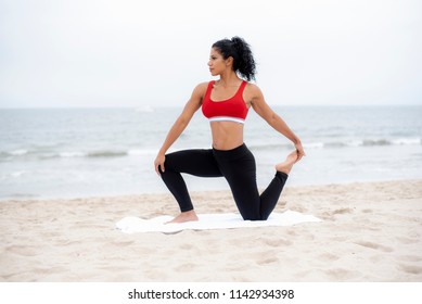 A Female Athlete Wearing Red Sports Bra And Black Leggings Stretches Quad Muscle Outdoors