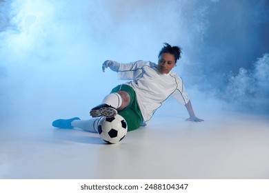 Female athlete in white and green attire performs football move amid smoke. - Powered by Shutterstock