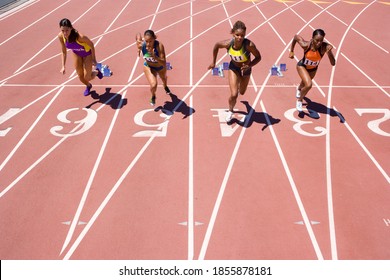 Female athletes setting off from their starting blocks at the start of a sprint race at an athletics competition at the track