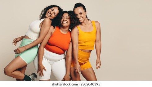 Female athletes smiling at the camera as they stand together in a studio, wearing fitness clothing. Group of young sports women expressing their love for sport, exercise and a health lifestyle. - Shutterstock ID 2302040395