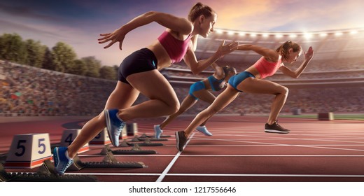 Female Athletes Sprinting. Three Women In Sport Clothes Run At The Running Track In Professional Stadium