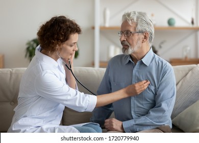 Female Attending Physician Holding Stethoscope Listening Old Patient During Homecare Visit. Doctor Checking Heartbeat Examining Elder Retired Man At Home. Seniors Heart Diseases, Cardiology Concept.