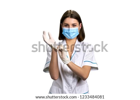Female attractive doctor puts on gloves. Pretty medical specialist wearing medical mask and white latex gloves on white background.