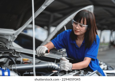 Female auto mechanic opens car hood to inspect engine damage and perform professional maintenance He wore a blue uniform and inspected and repaired his car in the workshop. - Powered by Shutterstock