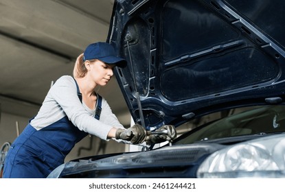 Female auto mechanic repairing, maintaining car. Beautiful woman working in a garage, wearing blue coveralls. - Powered by Shutterstock