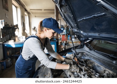 Female auto mechanic repairing, maintaining car. Beautiful woman working in a garage, wearing blue coveralls. - Powered by Shutterstock