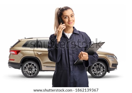 Female auto mechanic standing in front of suv and talking on a mobile phone isolated on white background