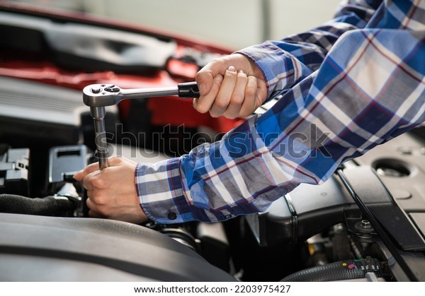 Female auto mechanic unscrewing a nut to replace a\
car spark plug.