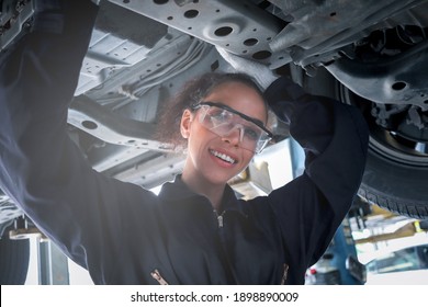 Female auto mechanic work in garage, car service technician woman check and repair customer car at automobile service center, inspecting car under body and suspension system, vehicle repair shop.