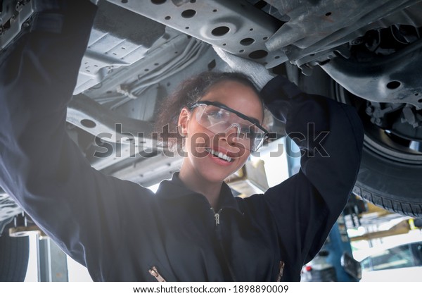 Female auto mechanic work in garage, car service\
technician woman check and repair customer car at automobile\
service center, inspecting car under body and suspension system,\
vehicle repair shop.