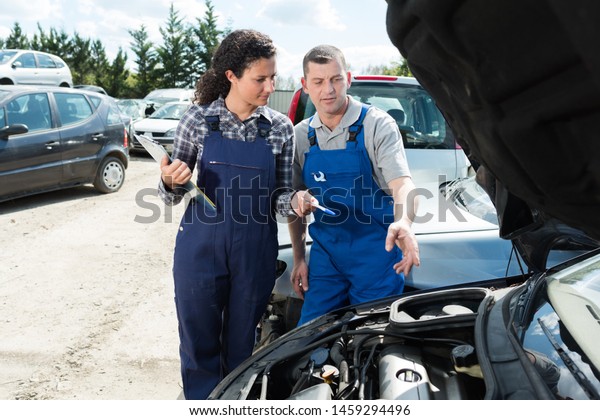 female auto mechanic working outdoors with\
mature male colleague