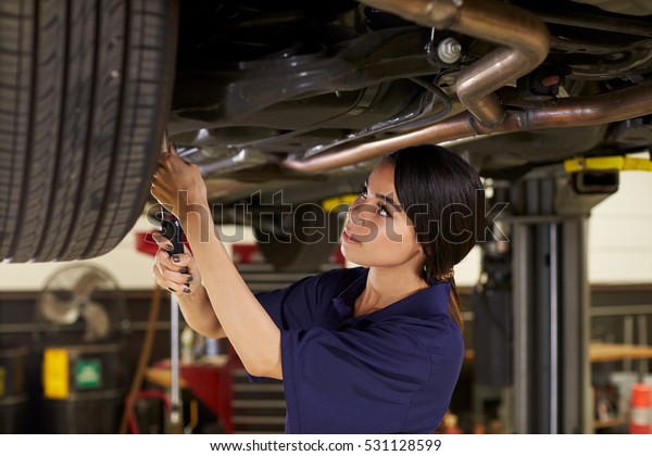 Female\
Auto Mechanic Working Underneath Car In\
Garage