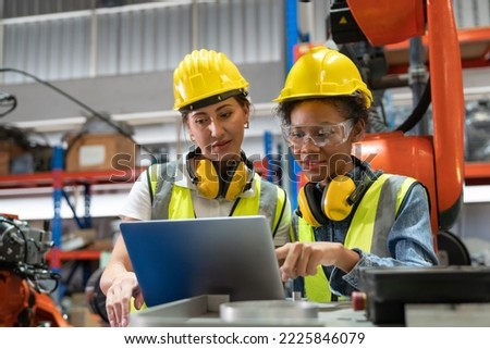 Female automation engineers in safety vest with yellow helmet using laptop for inspection new welding robot arm machine in industrial factory