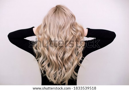 Female back with long, curly, natural blonde hair, in black dress, on grey background