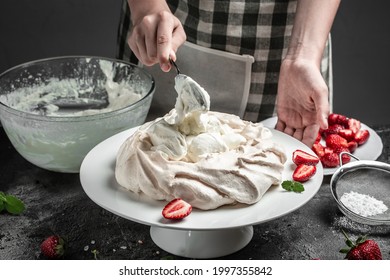 Female Baker Decorating Delicious Meringue Cake, Unfinished Pavlova Cake. Meringue With Topping With Whipped Cream And Strawberries. Culinary, Bakery, Food And People Concept.