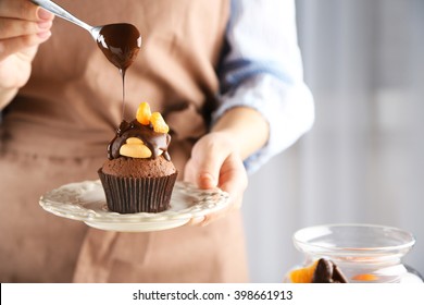 Female baker decorating tasty cupcake with slice of mandarin and chocolate on the table - Powered by Shutterstock