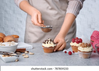 Female baker decorating tasty cupcake with cinnamon at table