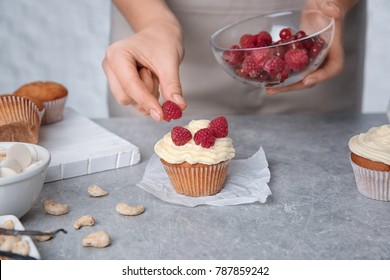 Female Baker Decorating Tasty Cupcake With Raspberries At Table