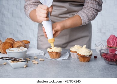 Female Baker Decorating Tasty Cupcake With Cream At Table