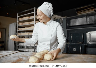 Female baker holding raw bun preparations before baking in oven - Powered by Shutterstock