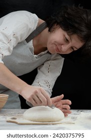 Female Baker making patterns on raw bread using a knife ot blade to shape the dough prior to baking. Manufacturing process of a bread at home