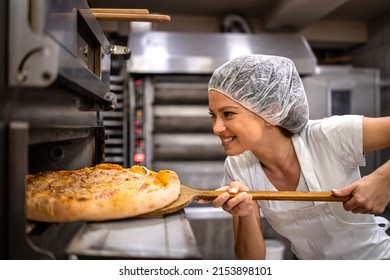 Female baker or restaurant chef in white uniform and hairnet checking baked pizza in the oven in pizzeria. - Shutterstock ID 2153898101