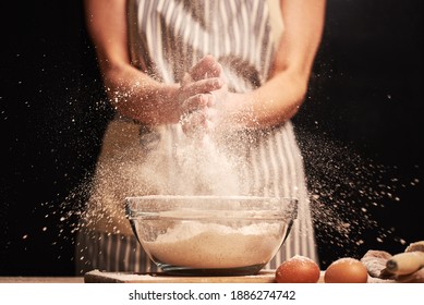 Female Baker Slapping Hands And Splashing Flour While Making Dough For A Loaf Of Bread With An Apron. Natural Homemade Ingredients. Eggs And Roller Visible In The Background.