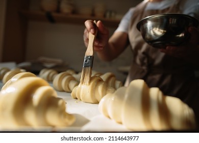 Female baker smears raw croissants with a brush in the yolk, the cooking process. - Powered by Shutterstock